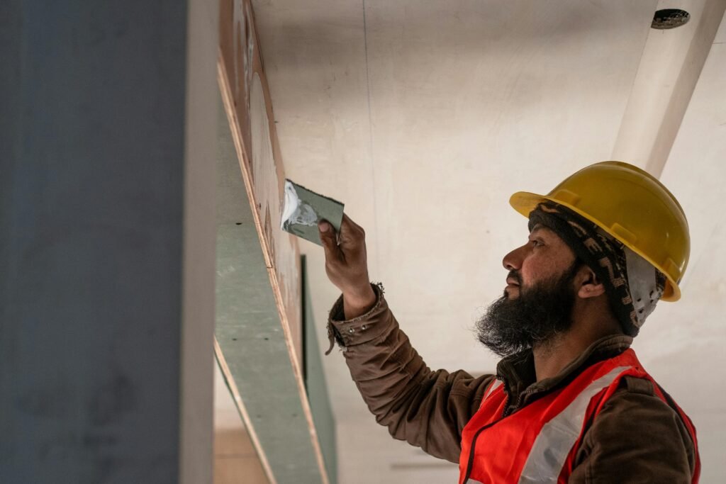 Construction worker in Delhi applies plaster to ceiling, showcasing renovation skills.