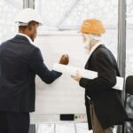 Two architects in hard hats working on a blueprint indoors, highlighting teamwork.